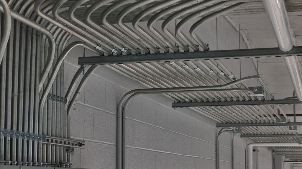 Rack of steel conduit runs bending across a block wall inside an industrial building wired by Adams Electric