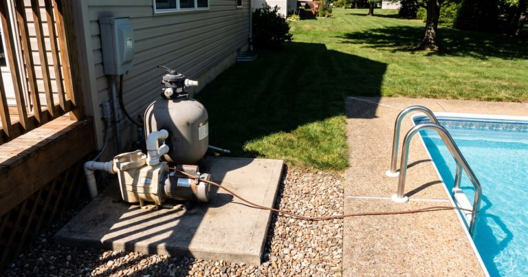 Pool pump, filter, and electrical disconnect beside an in-ground pool, with the copper bonding conductor running to the ladder handrails.